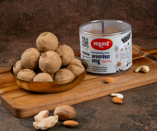 Ashwagandha Ladoo / Balls in a copper bowl with a container labeled 'Ashwagandha Ladoo' and Ladoobai's Brand on a wooden board.