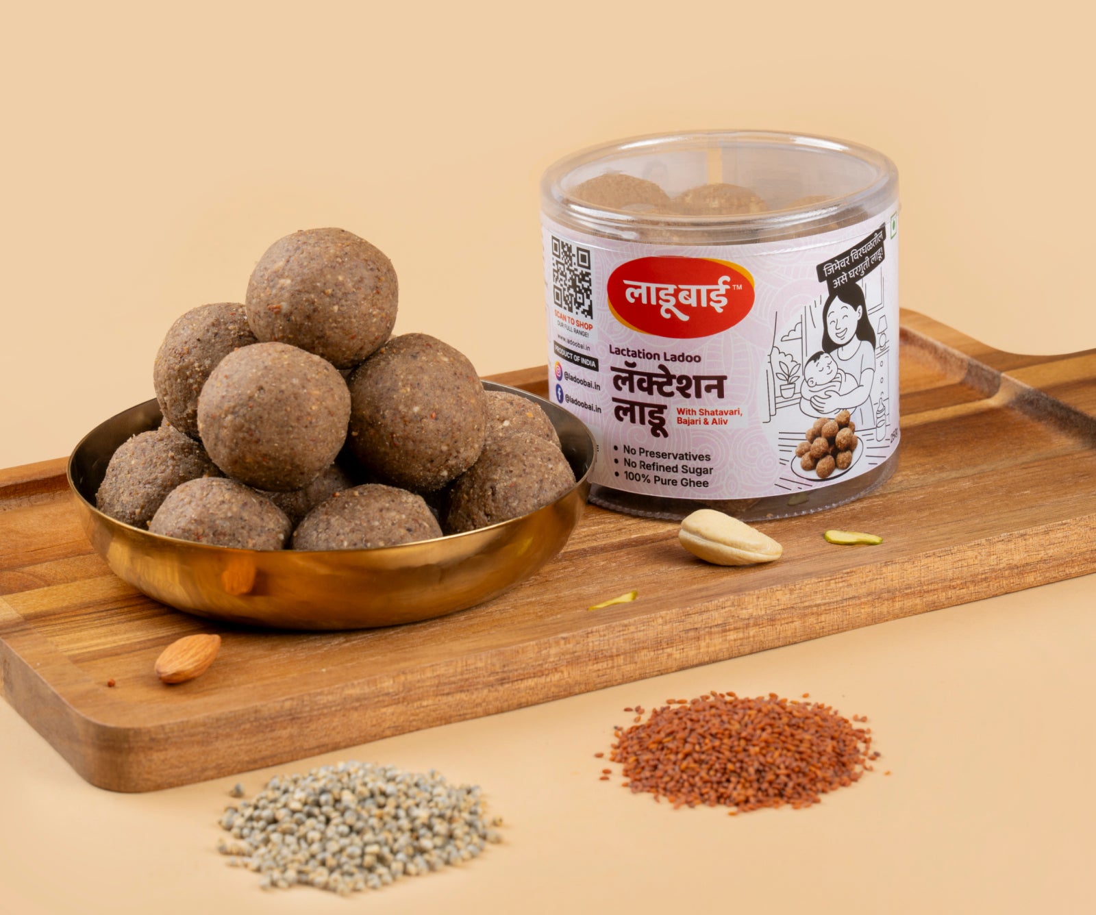 Light brownish Lactation Laddoos / Balls in a copper bowl with a container labeled 'Lactation Ladoo' and Ladoobai's Brand with an illustration of a lady with her newborn child, placed on a wooden board. Sprinkled ingredients/dry fruits around and wholegrain bajra and aliv on the side.