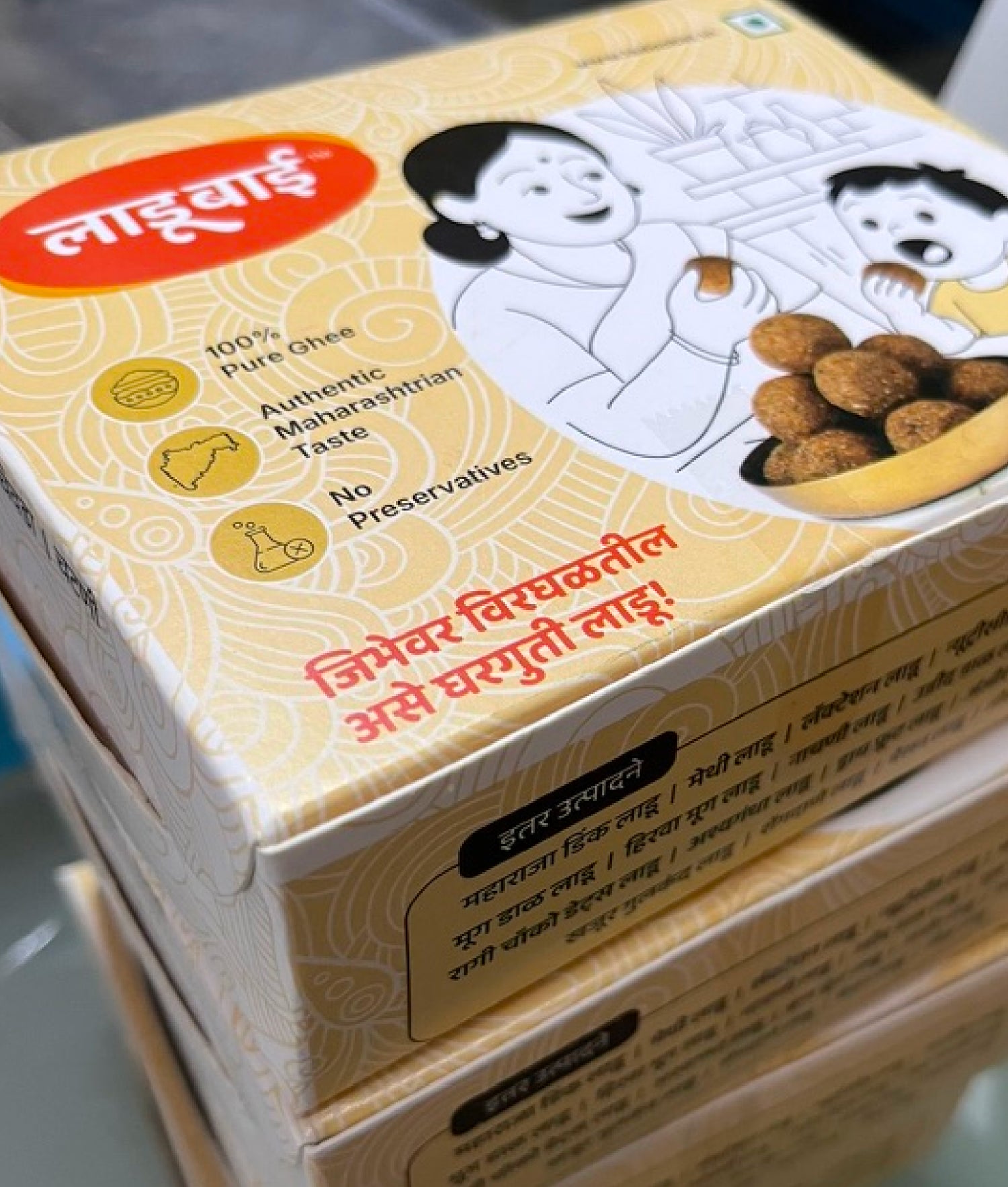 Branded Box of Ladoobai Ladoo Packaging with branding and product information on a yellow beige background. Owned by Ladoobai